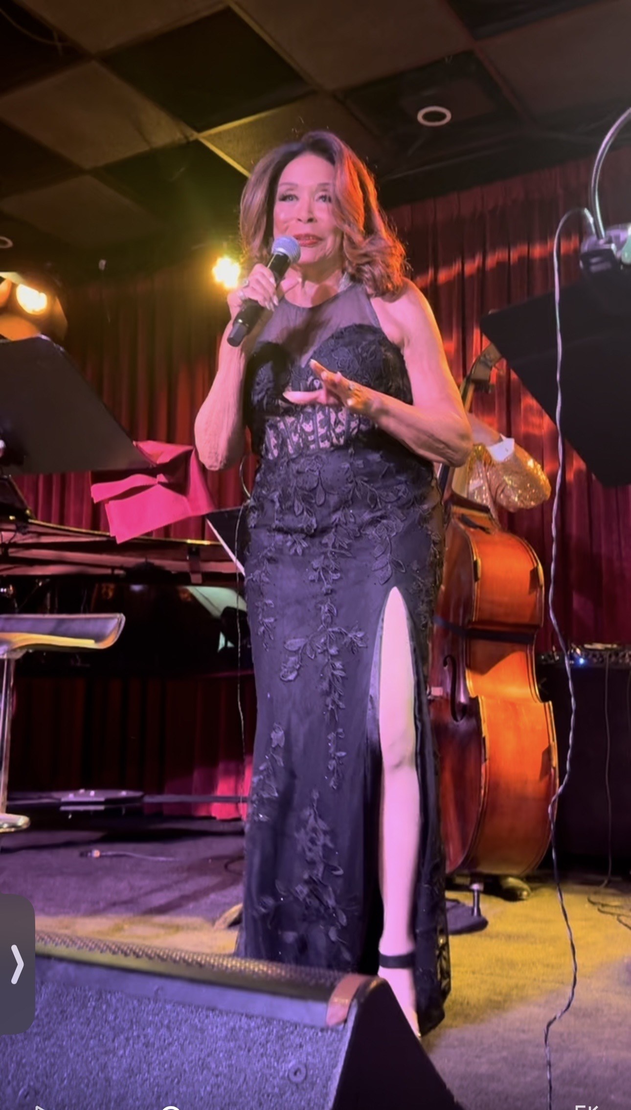 Freda Payne in a black lace gown with a thigh-high slit, upright bass behind her
